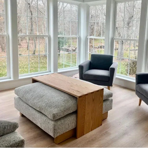 ottoman coffee table, ottoman table, wood ottoman overlay. Modern living room with large windows, gray furniture, and a wooden coffee table.