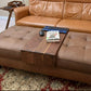 luxury wood ottoman cover table sitting over a leather ottoman with various everyday items sitting on the ottoman table